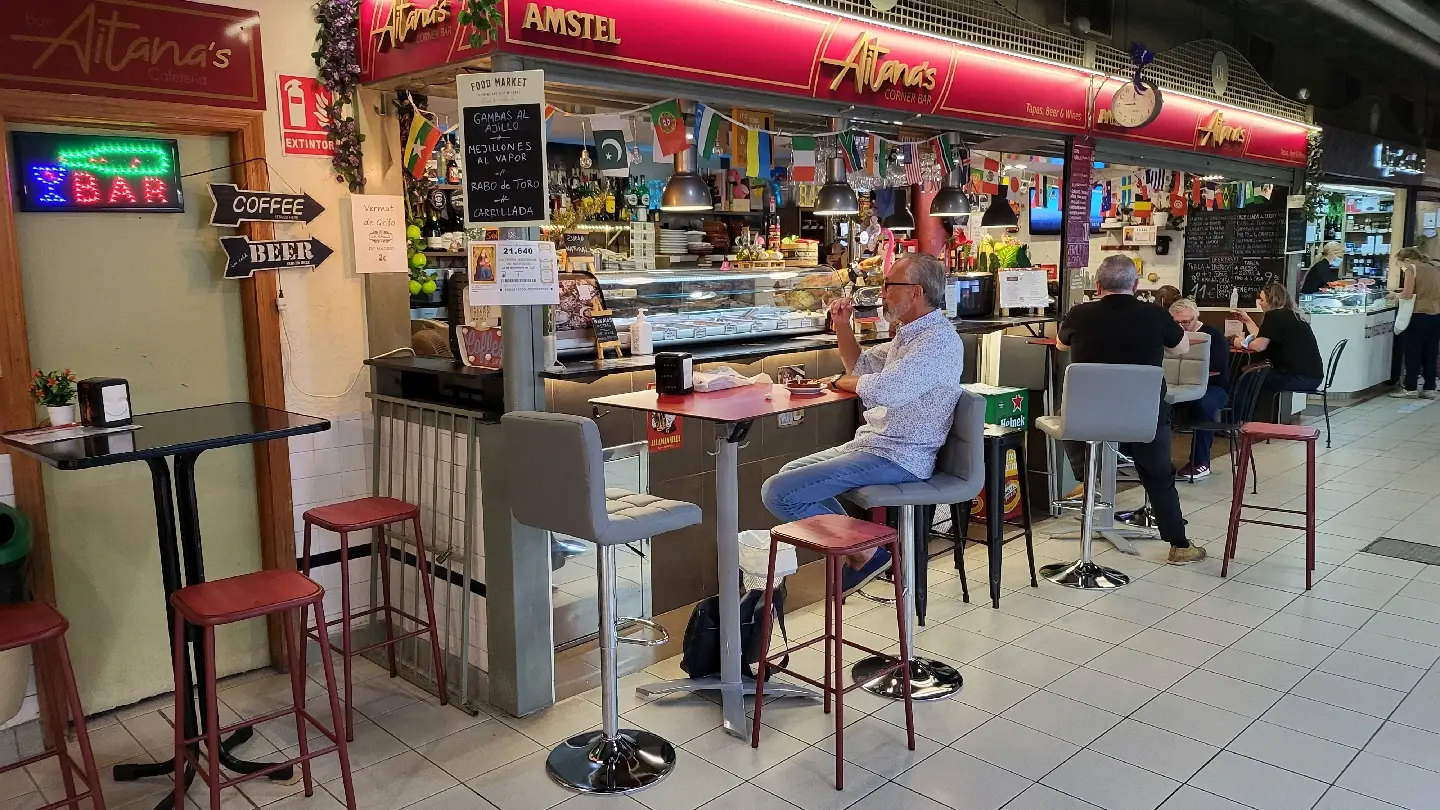 El puesto de Aitana's en el Mercado Central: el rótulo granate, la barra con taburetes y las banderas